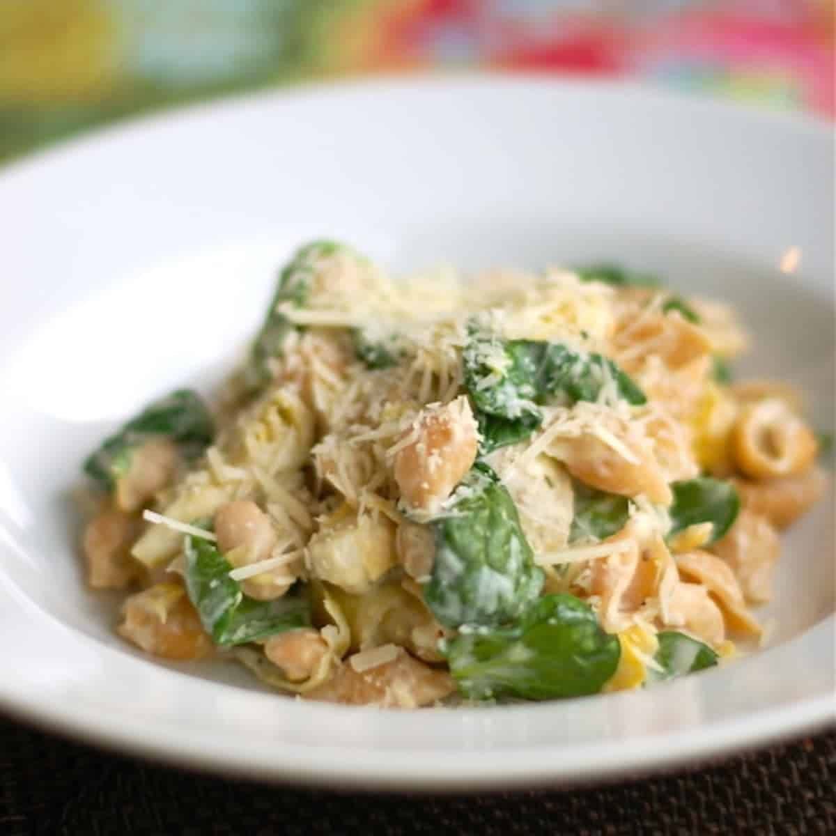 Spinach artichoke pasta in a white bowl.
